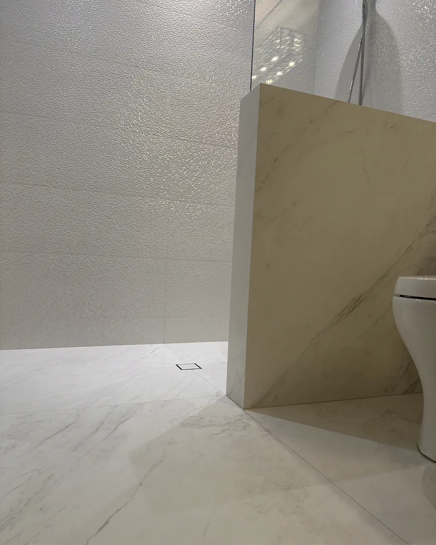 Finished white marble-look shower with a mitered pony wall and square drain