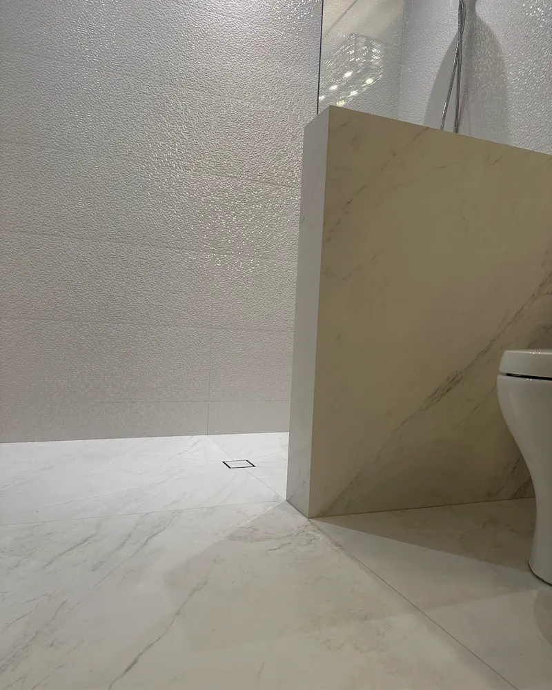 Finished white marble-look shower with a mitered pony wall, square drain and textured wall tile