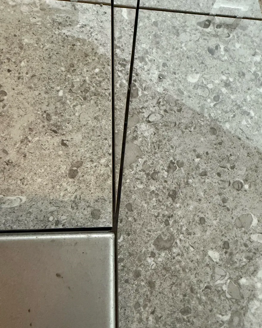 Stone-look tile meeting a metal inlay with hairline joints