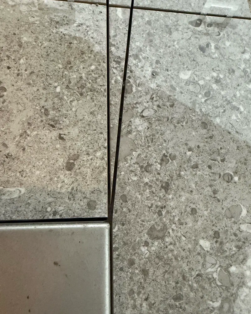 Tight epoxy grout joint between natural stone tile and metal transition in a Venice FL home