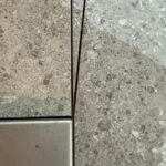 Stone-look tile with hairline joints meeting a metal inlay, by Floors of Glory